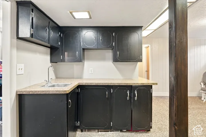 Kitchen area featuring dark cabinetry, speckled laminate countertops, a stainless steel undermount sink with a gooseneck faucet, and a wooden support pillar