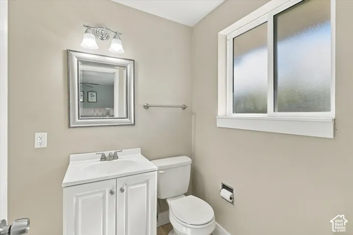 White vanity cabinet with integrated countertop, dual-light wall fixture, framed mirror, and sliding privacy-glass window