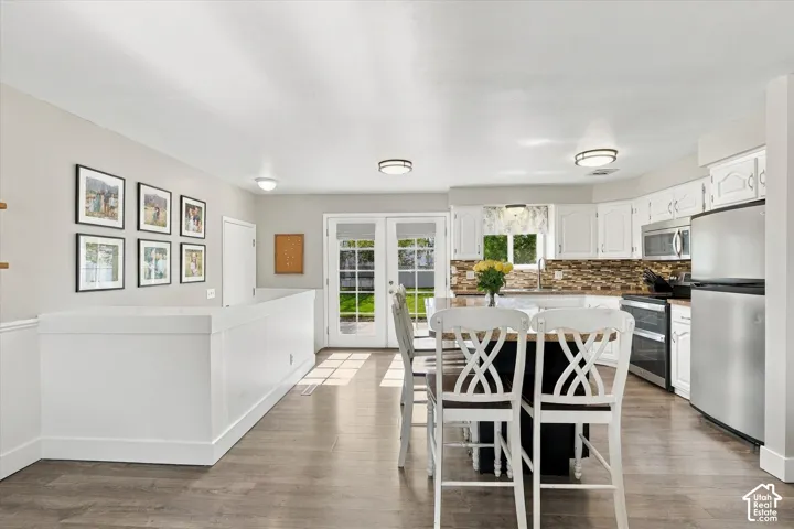 Kitchen featuring white cabinetry, wood-finish flooring, stainless steel appliances, a tile backsplash, and double glass doors