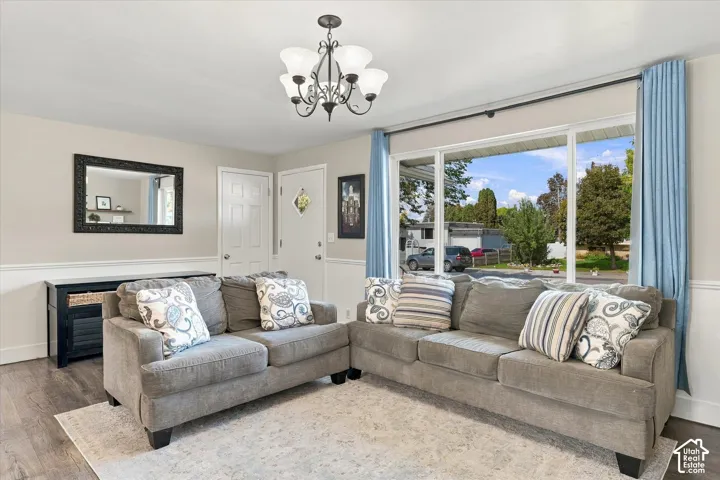 Living area featuring wood-finish flooring, a multi-light chandelier, a picture window, and wainscoting