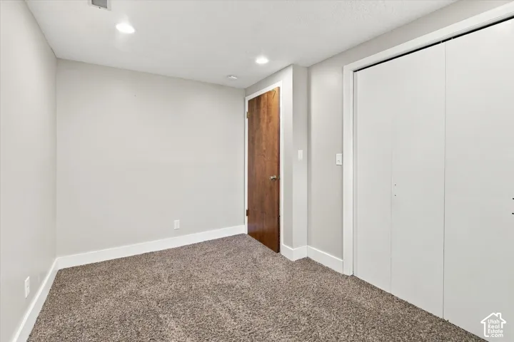 Neutral-toned interior room featuring wall-to-wall carpeting, recessed ceiling lighting, a wood-finish interior door, and a white double-door closet