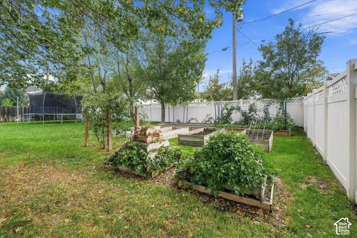 Backyard featuring multiple raised garden beds, mature trees, and a white vinyl privacy fence with lattice detailing