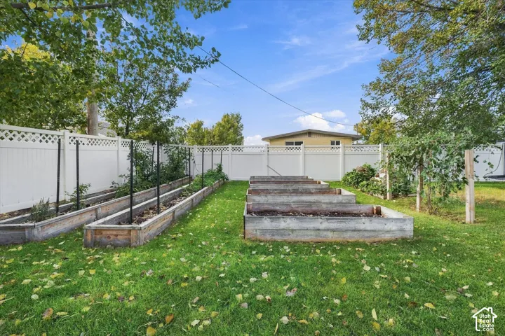 Backyard featuring raised wooden garden beds, white privacy fencing with lattice detail, and a lawn area