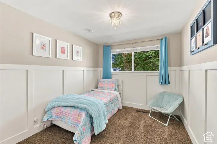 Bedroom featuring wall-to-wall carpeting, wainscoting, and a central crystal flush-mount light fixture