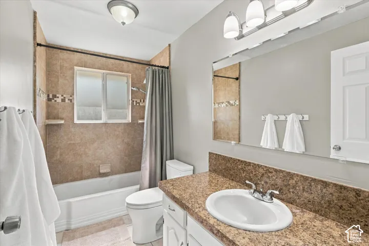 Bathroom featuring a white vanity with a composite countertop and undermount sink, large wall-mounted mirror, ceramic tile shower surround with decorative inlay, and chrome-finish light fixtures