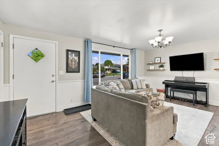Living area featuring wood-finish flooring, two-tone walls with chair rail molding, large picture window, and a multi-arm chandelier with glass shades