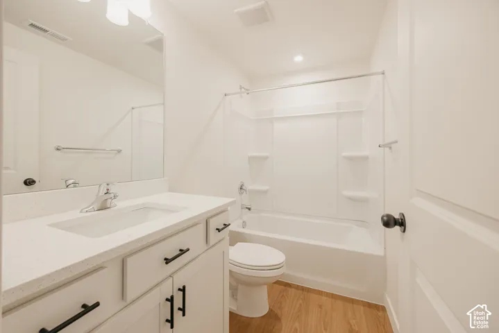 Bathroom featuring a vanity with a light-toned countertop, integrated basin, and matte black hardware, paired with a white tub-shower combination and wood-finish flooring
