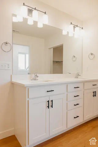 Dual-sink vanity featuring white cabinetry, matte black hardware, stone-finish countertops, and dual wall-mounted light fixtures