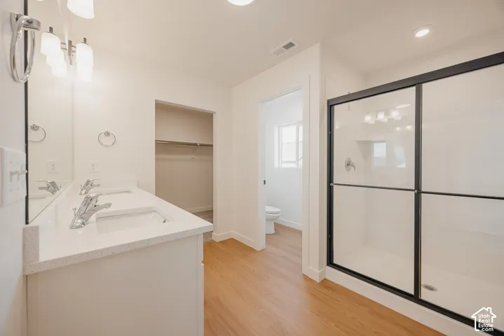 Dual vanity with stone-composite countertop, glass-enclosed shower with matte black frame, wood-finish flooring, and built-in closet storage