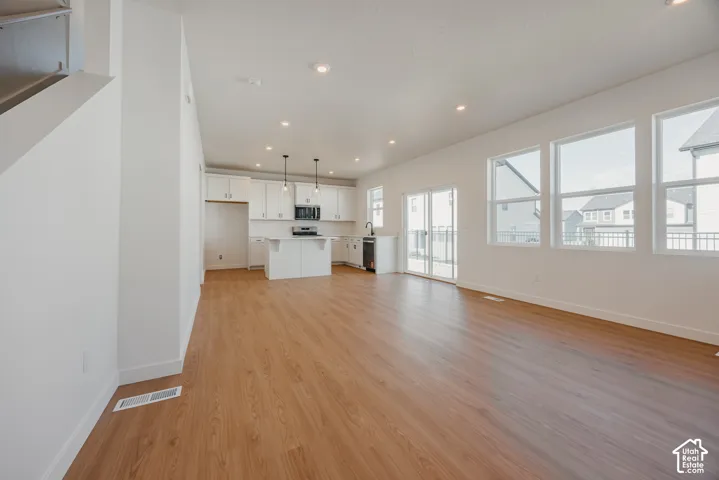 Open-concept interior featuring wood-finish flooring, recessed lighting, white cabinetry, a central island, and large windows
