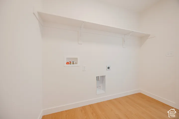 Laundry area featuring wood-finish flooring, white wall shelving, and dedicated water and electrical hookups