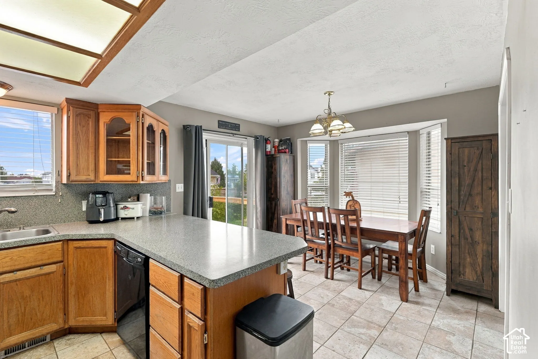Kitchen and dining area featuring natural wood cabinetry, stone-texture countertops, tile flooring, a multi-pane bay window, and a sliding glass door