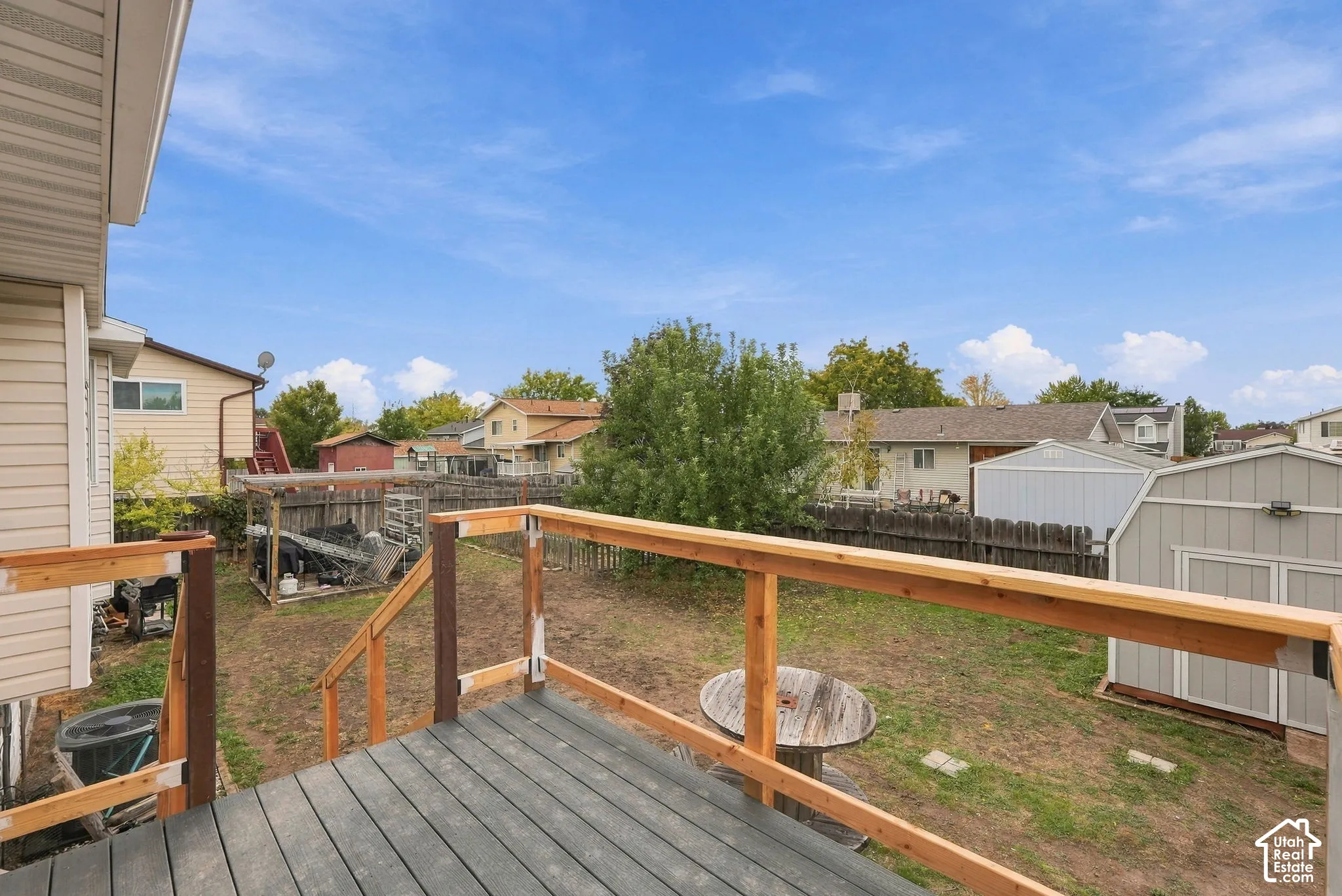 Elevated wood-plank deck featuring a natural wood railing and an expansive, fenced backyard with a storage shed