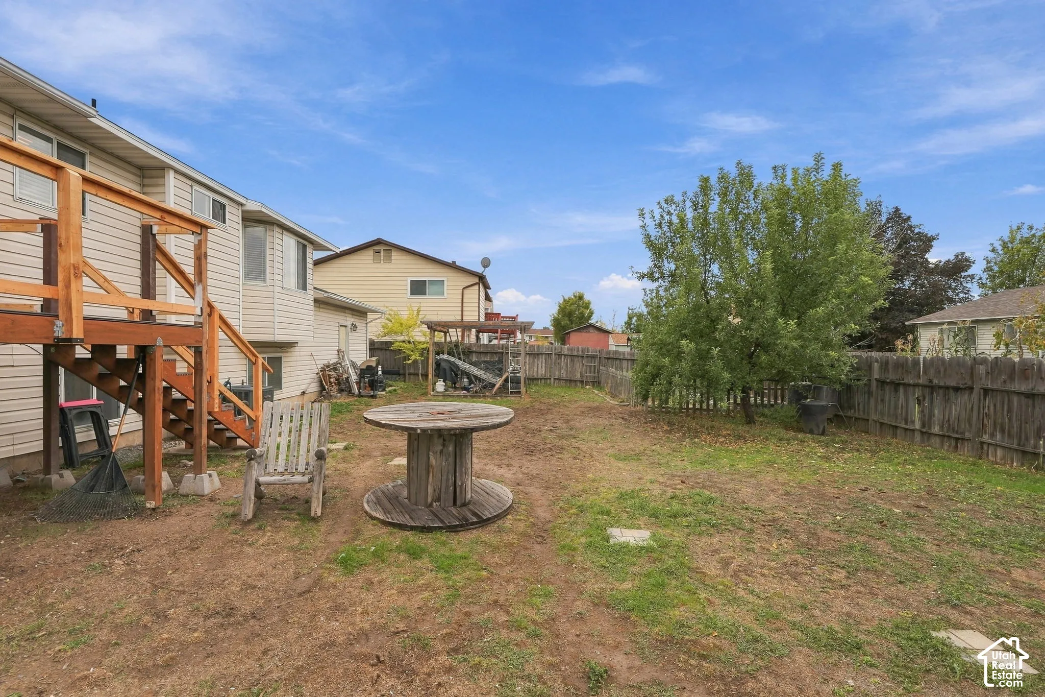 Rear exterior featuring a raised wooden deck with railings, a wood privacy fence, and mature trees