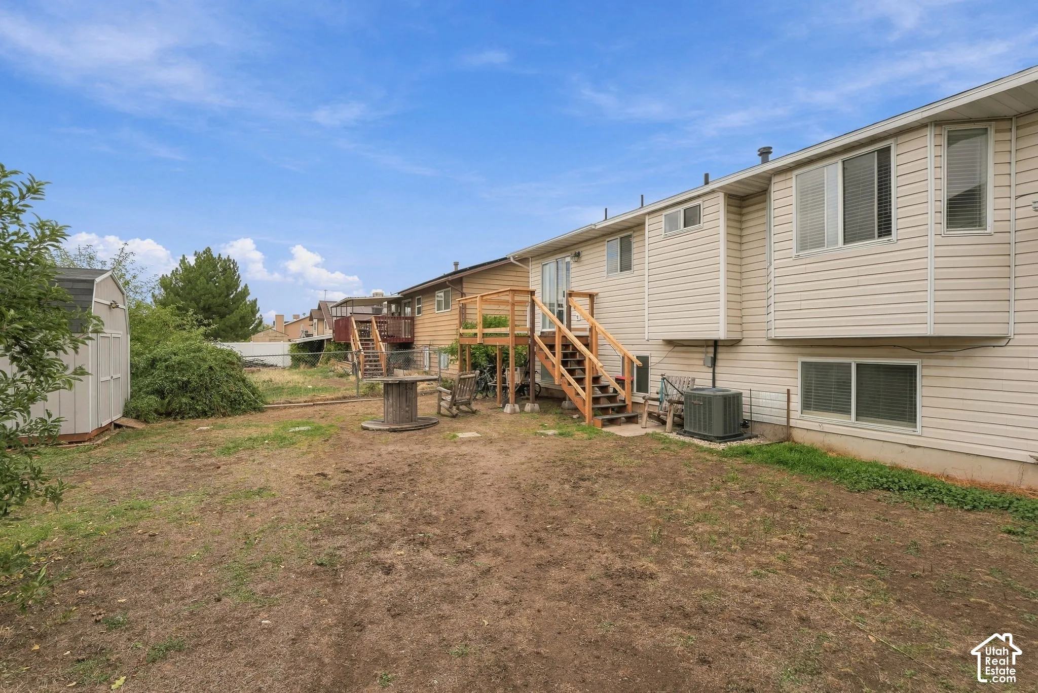 Rear exterior featuring light-colored horizontal siding, a raised wooden deck with staircase, multiple multi-pane windows, and a detached storage structure