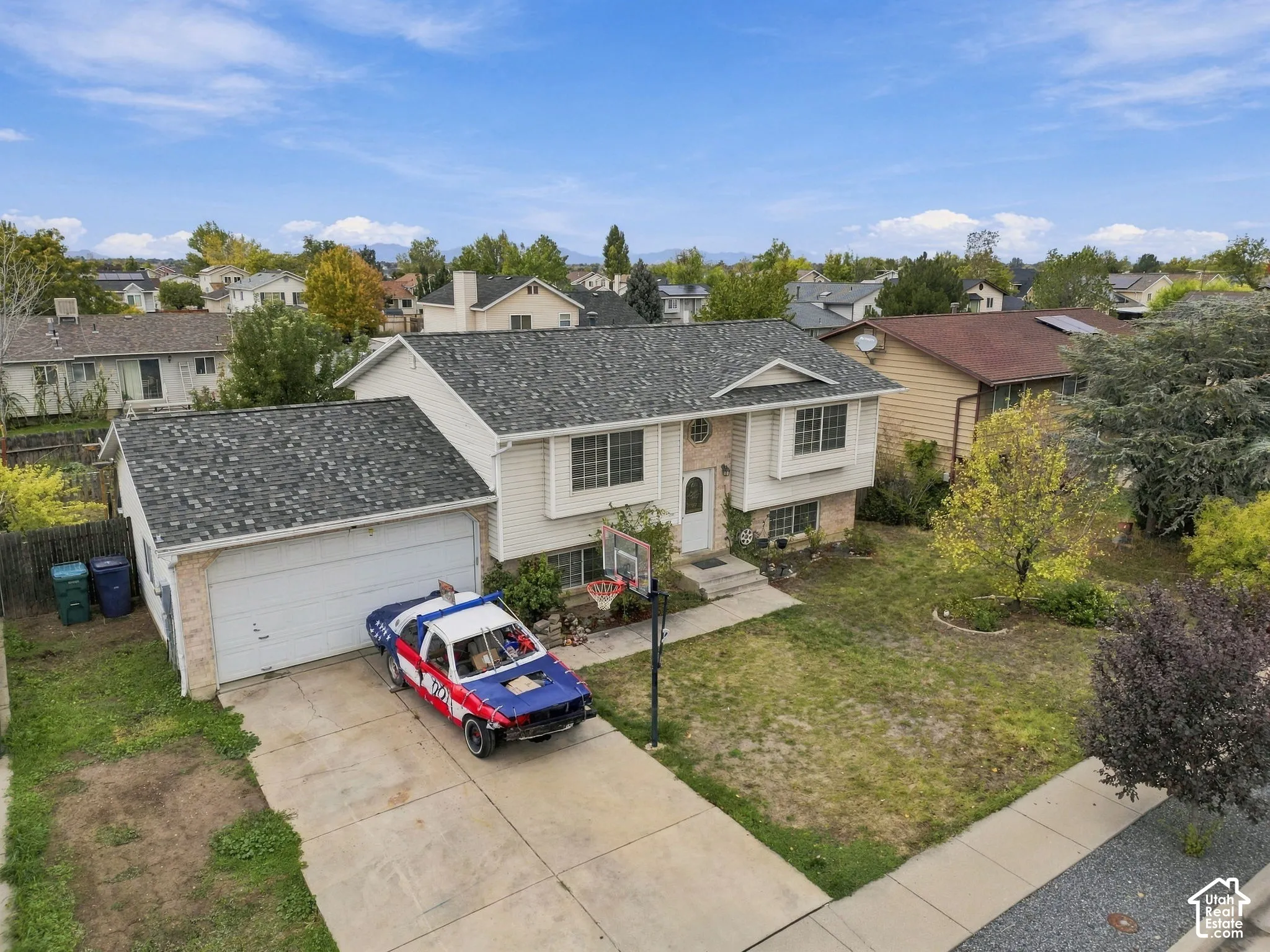 Split-level exterior featuring light-colored horizontal siding, brick facade accents, a multi-pitched roof with asphalt shingles, and an attached two-car garage