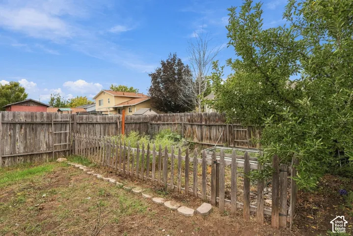 Fenced backyard featuring wood perimeter fencing, a picket-style garden enclosure, raised garden beds, and mature trees