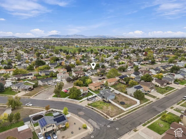 Aerial perspective of a corner lot property featuring a fenced backyard, concrete driveway, and mountain horizon backdrop