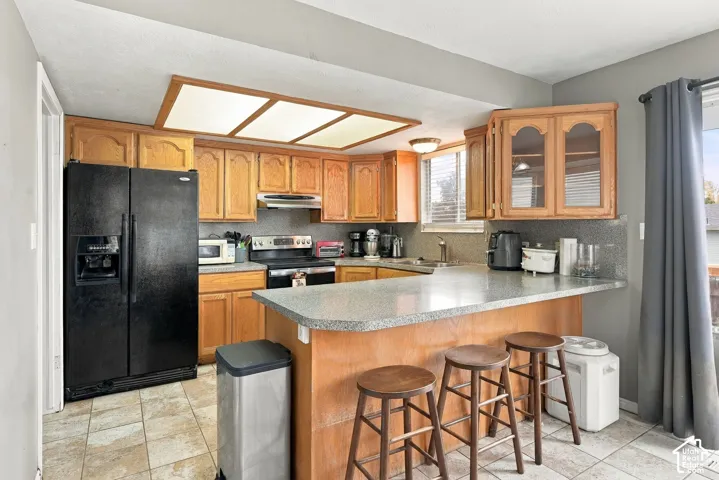 Kitchen featuring oak cabinetry with glass-panel upper doors, stone-composite countertops, breakfast bar, and integrated recessed panel lighting