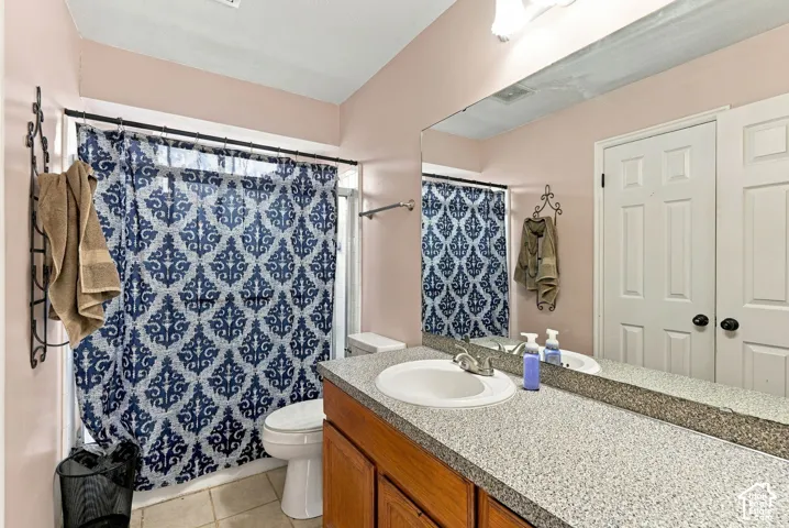 Bathroom featuring wood-finish cabinetry, stone-texture countertop, integrated oval basin, full-width vanity mirror, and ceramic tile flooring