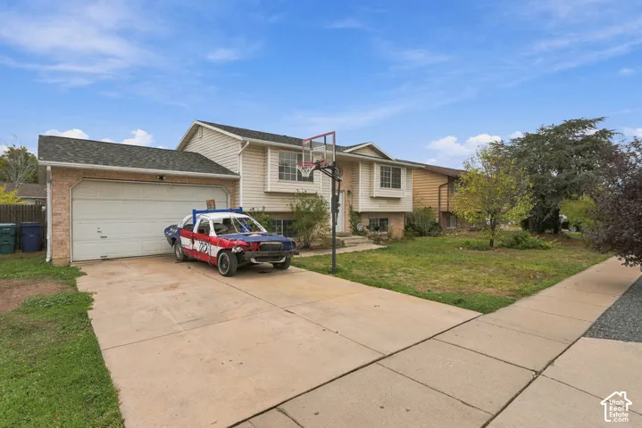 Split-level exterior featuring light-toned vinyl siding, a brick facade, an attached two-car garage, and a concrete driveway