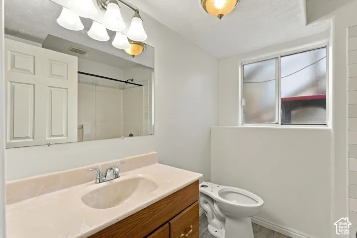 Bathroom featuring a wood-finish vanity with a molded countertop and sink, chrome-finish double-handle faucet, wall-to-wall mirror, and privacy-glass window