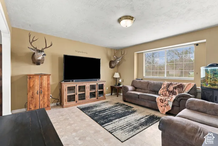 Spacious living area featuring neutral-toned walls, a large picture window, textured ceiling, and tile flooring
