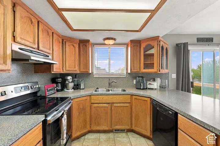Kitchen featuring warm-tone wood cabinetry, speckled laminate countertops, a dual-basin stainless steel sink, a stainless steel range with overhead vent hood, and recessed ceiling lighting