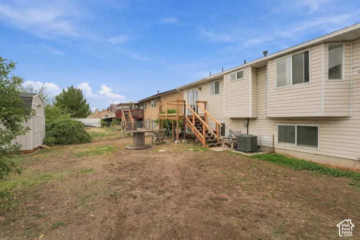 Rear exterior featuring light-colored horizontal siding, a raised wooden deck with staircase, multiple multi-pane windows, and a detached storage structure