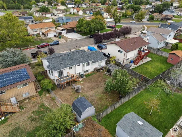 Fenced backyard featuring a raised wooden deck, pergola, mature trees, and a detached storage shed