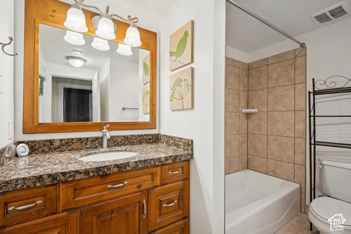 Wood-finish vanity with a stone-surfaced countertop, integrated basin, and matching framed mirror, complemented by a tile-surround bathtub and three-bulb vanity lighting