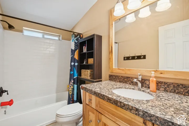Bathroom featuring a wood vanity with a stone-finish countertop, white undermount sink, built-in wooden-framed mirror, and a tiled tub-shower enclosure