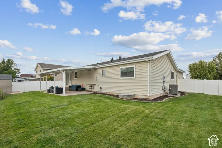 Expansive backyard featuring a manicured lawn, a covered concrete patio, and white vinyl privacy fencing
