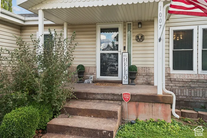 Covered entryway featuring light-colored horizontal siding, a concrete porch, decorative scalloped fascia trim, and masonry foundation detailing