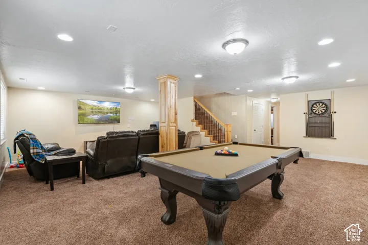 Open-concept interior featuring recessed lighting, a wood-wrapped support pillar, carpeted flooring, and a staircase with metal balusters