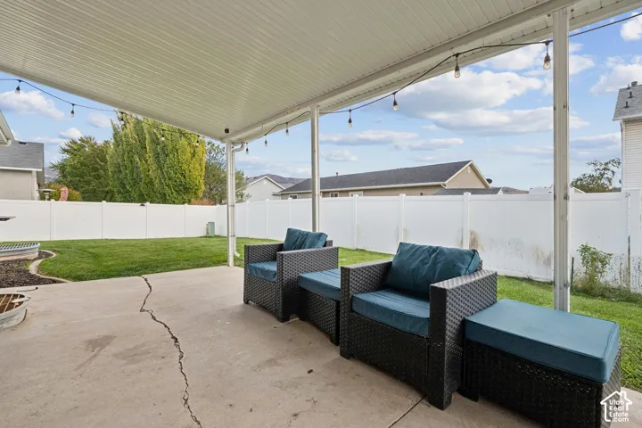 Covered concrete patio with overhead string lighting, encompassing a fenced backyard featuring a level lawn