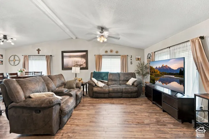 Vaulted ceiling featuring a central ceiling fan with integrated lighting, wood-finish flooring, and multiple windows with drapery hardware