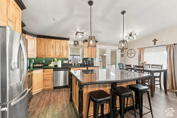 Kitchen featuring natural wood cabinetry with black crown molding, a central island with a solid-surface countertop, stainless steel appliances, and dual pendant lighting
