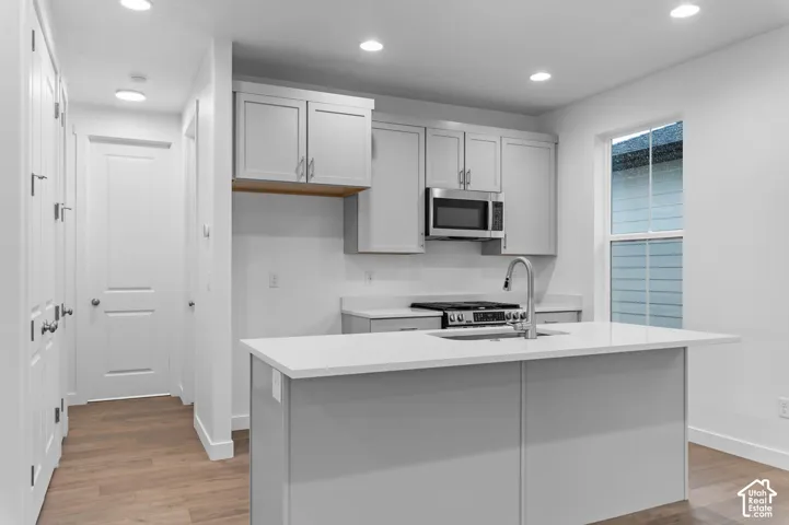 Kitchen featuring shaker-style cabinetry, a central island with a solid-surface countertop, an undermount sink with a gooseneck faucet, built-in microwave, and wood-finish flooring