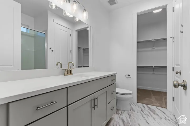 Grey vanity cabinetry with a white countertop and integrated sink, polished metal hardware, multi-light fixture, and patterned tile flooring
