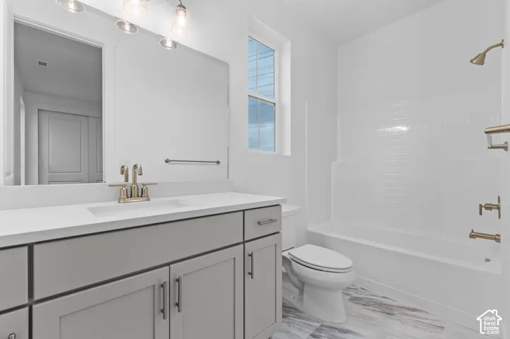Bathroom featuring a grey shaker-style vanity, white stone-composite countertop, metallic fixtures, and a tub-shower combination with white subway tile surround