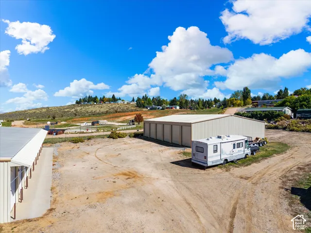 Large metal storage building with multiple roll-up doors, extensive unpaved lot, and additional metal structure with individual storage units