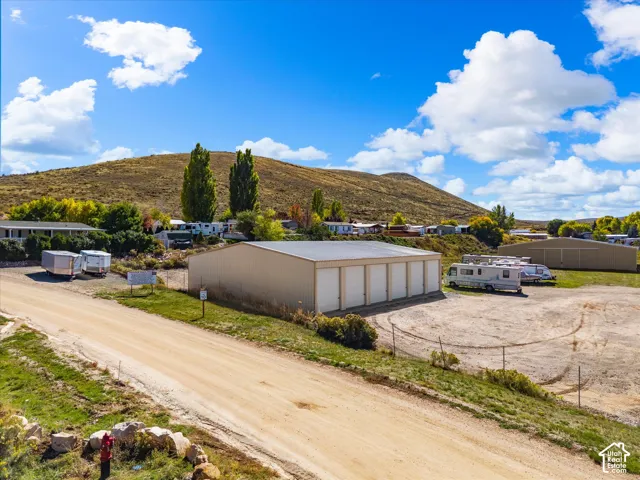 Warehouse structure with multiple roll-up doors, an expansive unpaved lot, and a surrounding natural landscape