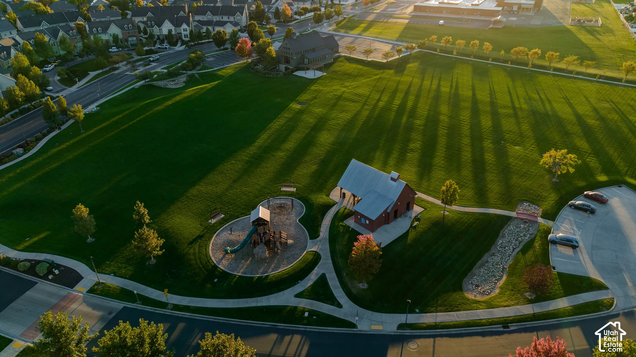 Expansive green space featuring a playground, paved walking paths, a stone-lined drainage area, and a structure with a metal roof