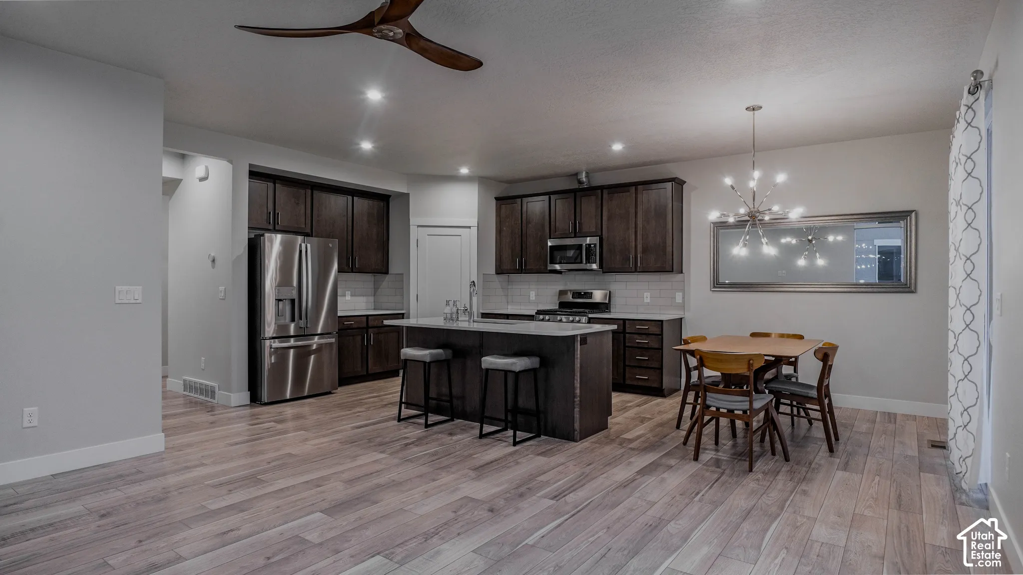 Open-concept kitchen featuring dark wood cabinetry, an island with quartz countertops, stainless steel appliances, recessed lighting, and LVP flooring