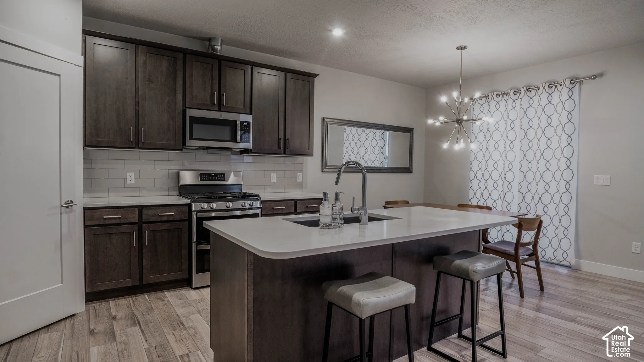 Kitchen featuring dark-finish cabinetry, a central island with quartz countertops, stainless steel appliances, a white subway tile backsplash, and LVP flooring