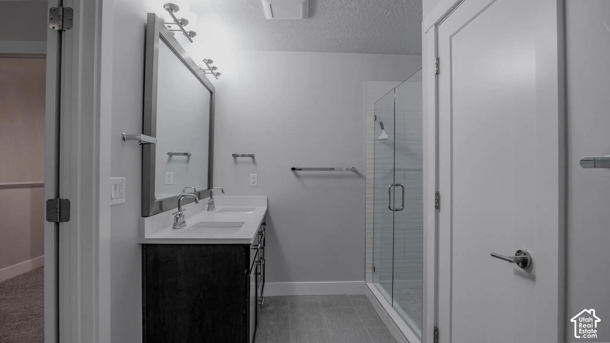 Dual-sink vanity with a quartz countertop, full-width framed mirror, glass-enclosed shower with subway tile surround, and tile flooring