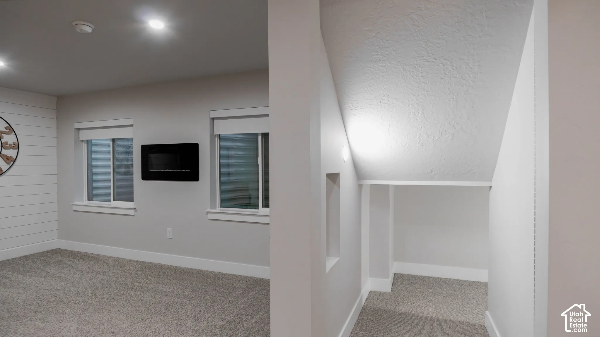 Horizontal shiplap accent wall, wall-mounted electric fireplace, recessed ceiling lighting, and custom under-stair storage nook with carpeted flooring