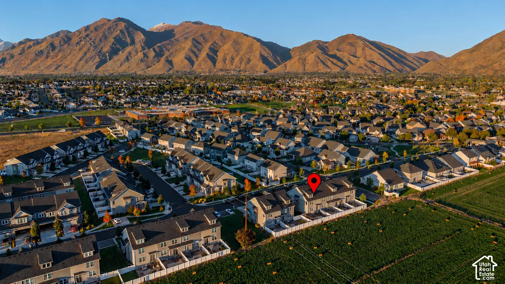 Aerial perspective of multi-level residential structure featuring a neutral exterior facade, gabled rooflines, and white perimeter fencing, set against a backdrop of mountain ranges