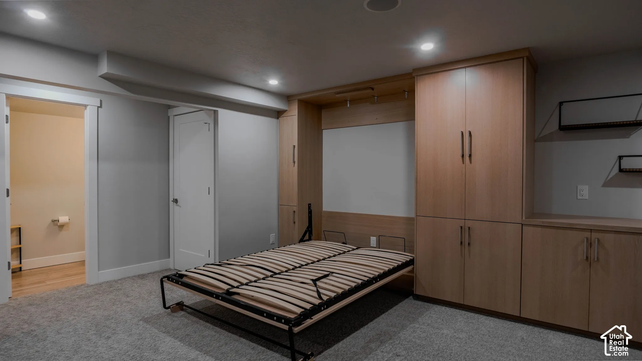 Built-in cabinetry with wood-finish doors, integrated wall bed system, recessed ceiling lighting, and neutral carpeting